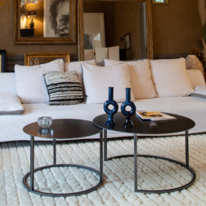 Table basse Eclypse en acier, design épuré, mise en scène dans un salon moderne avec coussins et décorations.