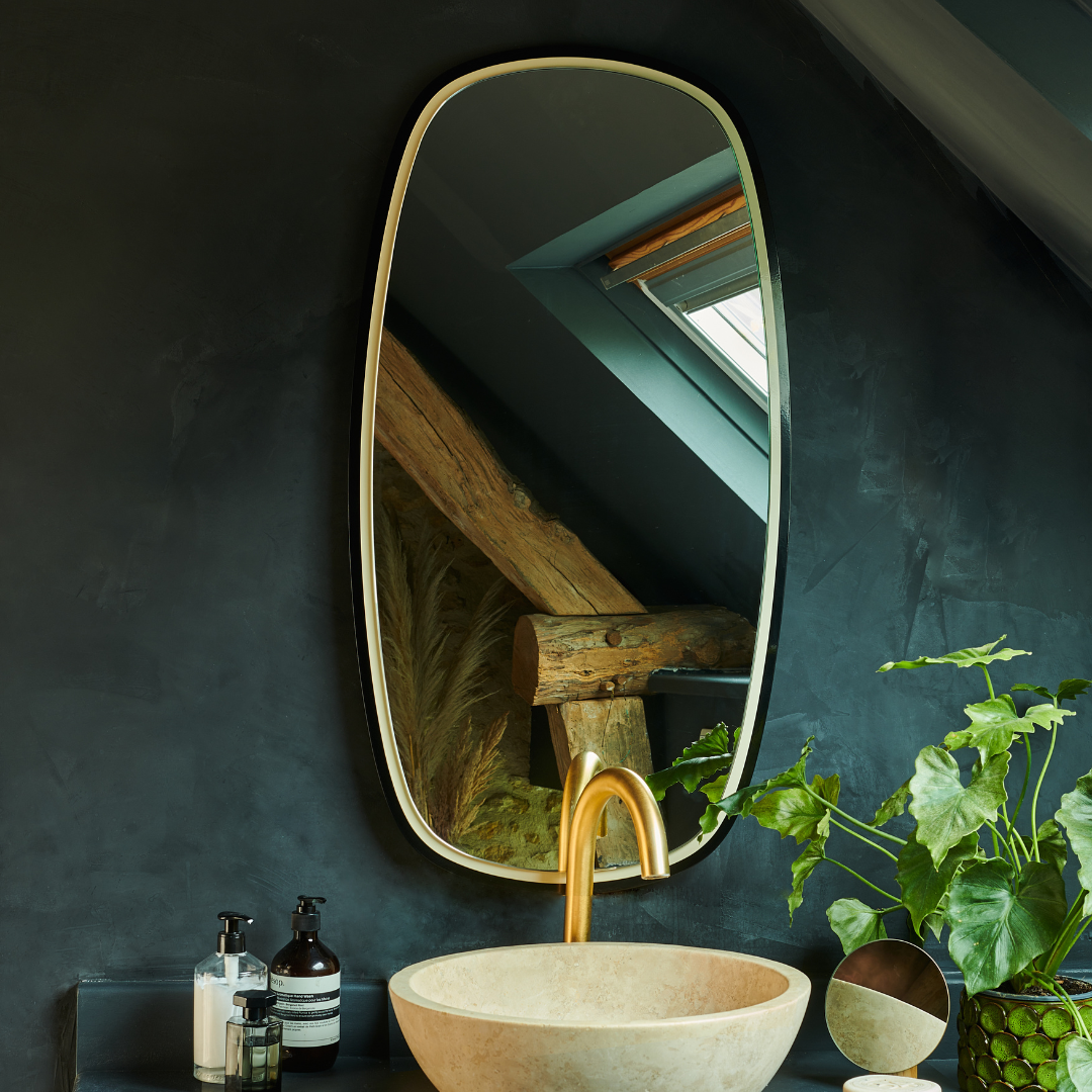 Miroir Héra ovale avec finition moderne, suspendu au-dessus d'un lavabo en pierre dans une salle de bain contemporaine.