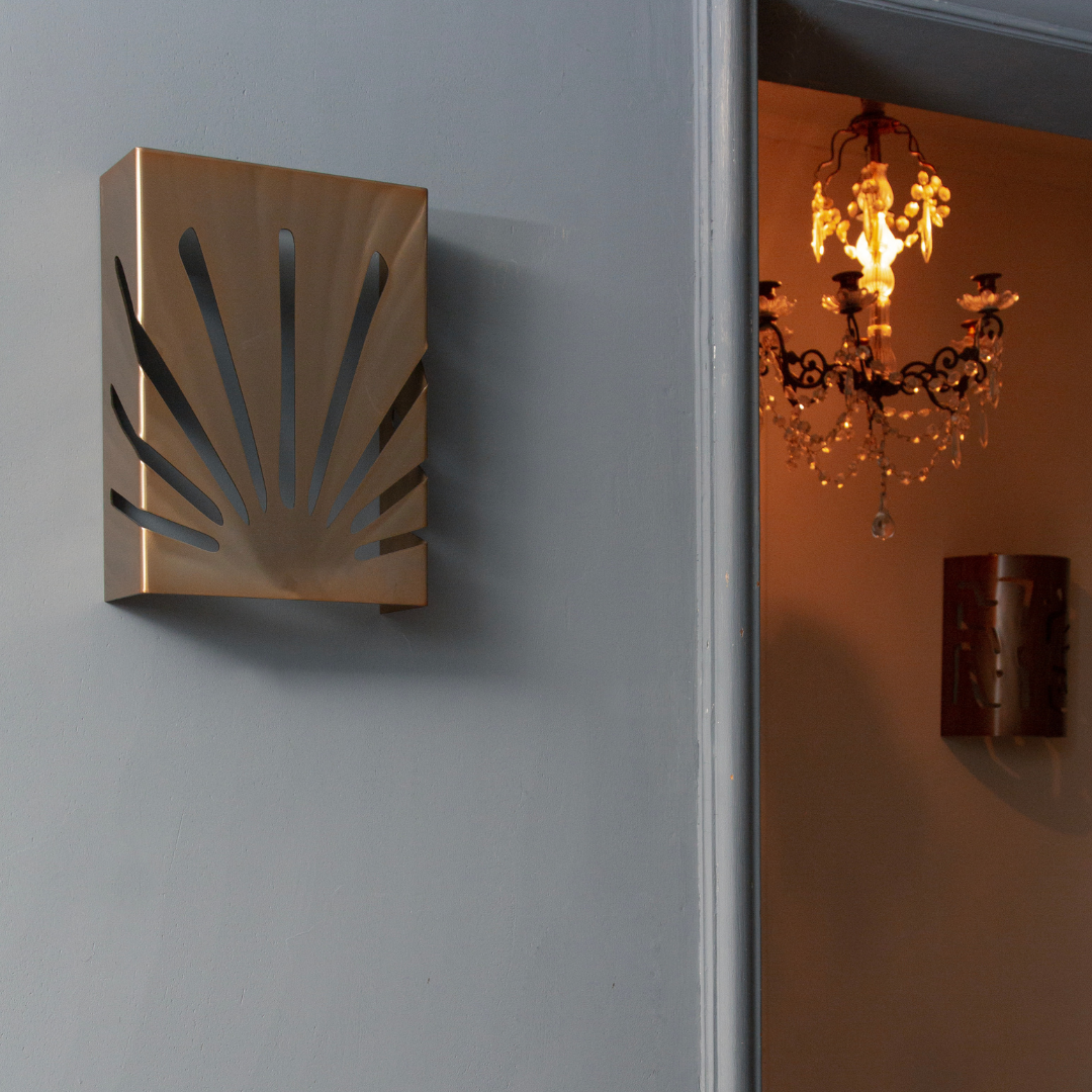 Applique en acier avec design moderne évoquant des rayons de soleil, accrochée sur un mur gris, éclairant un intérieur élégant.