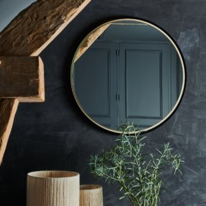 Miroir Héra rond avec cadre noir et doré, sur fond de mur sombre, associé à des éléments de décoration contemporaine.