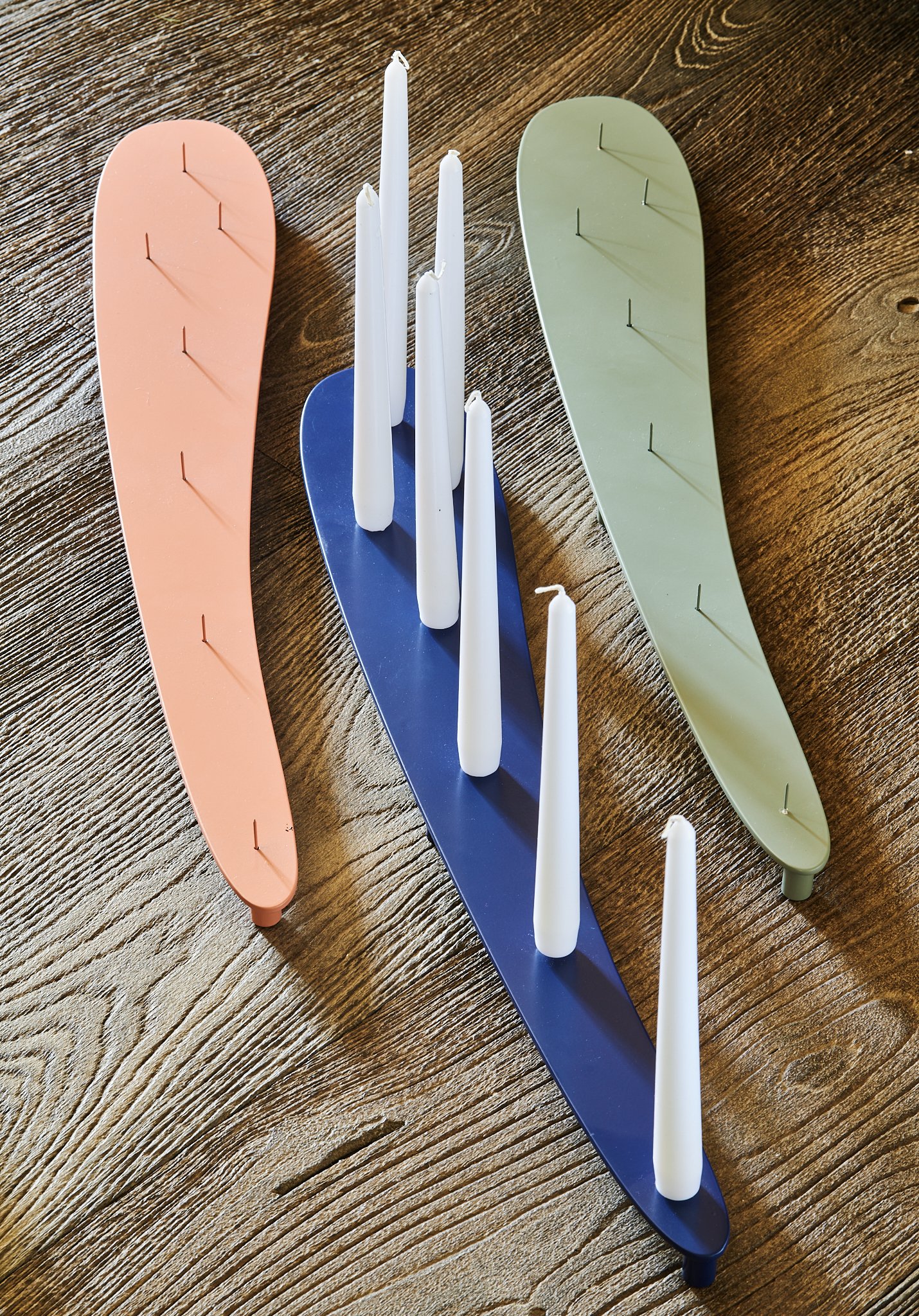 Bougeoir design Aphrodite en acier, coloris pastel, avec bougies blanches sur table en bois. Fabriqué en France par Atelier Héphaïstos.