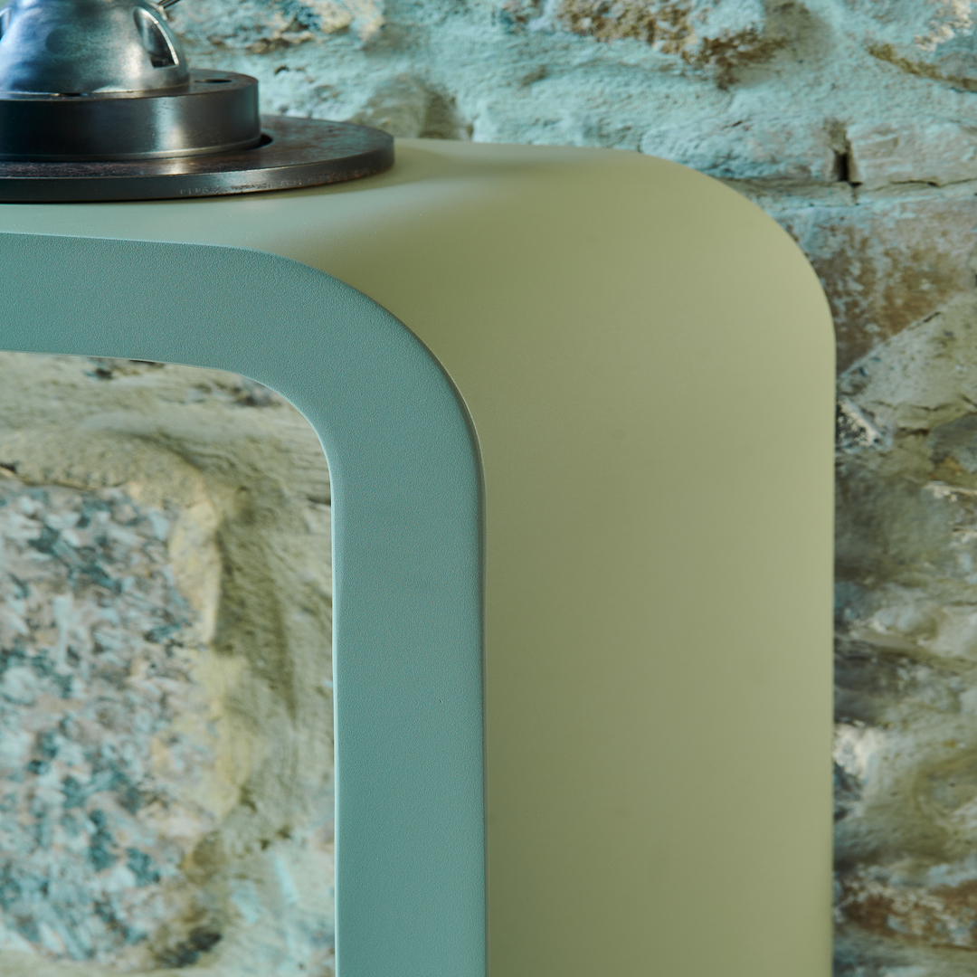 Détail d'une console en acier aux angles arrondis, sur fond de mur en pierre. Design contemporain et finition soignée.