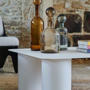 Table basse en acier blanc avec bouteilles décoratives, dans un intérieur moderne en pierre. Fabriqué par Atelier Héphaïstos.