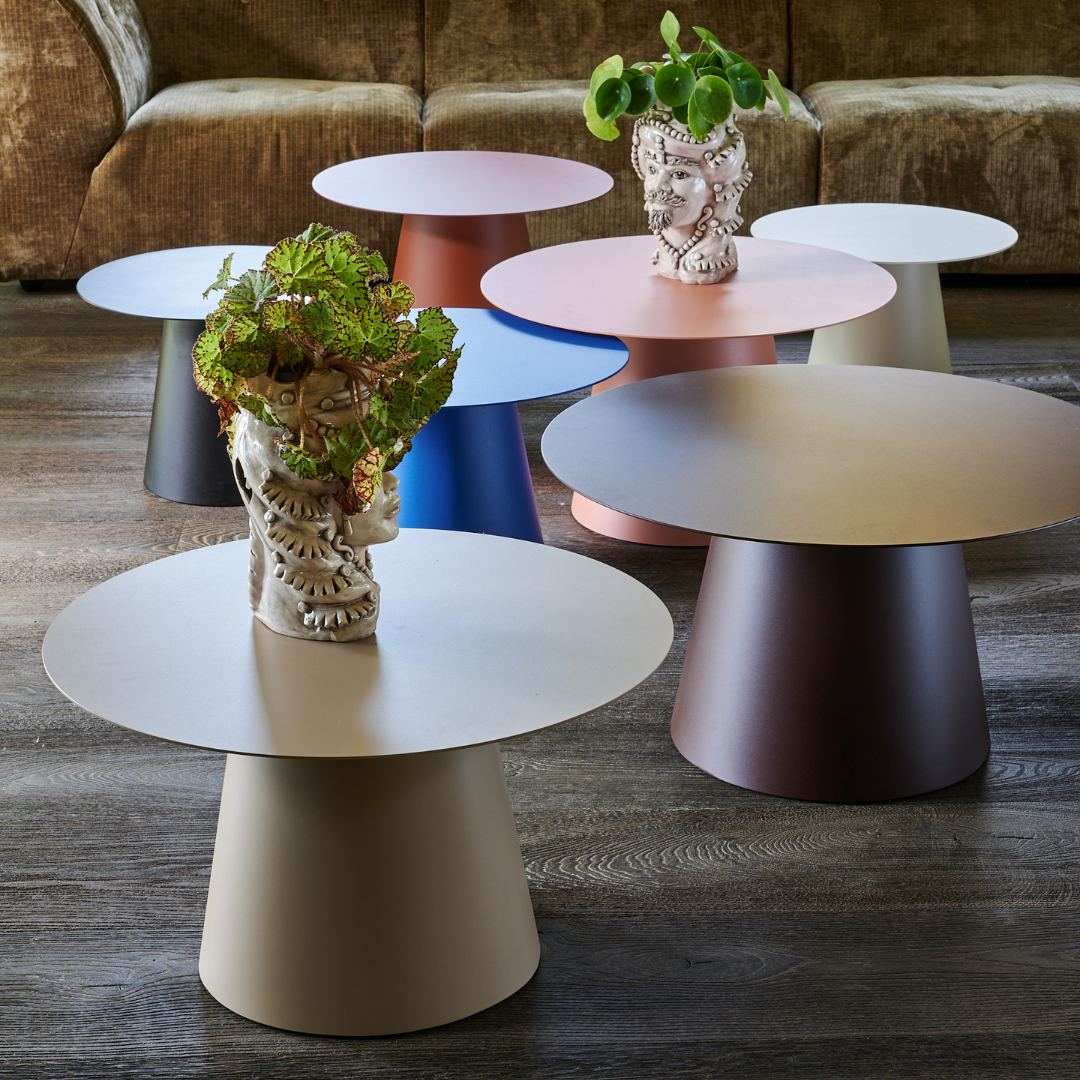 Table basse Lombok en acier aux couleurs variées, présentée avec des pots de plantes sur une surface en bois.