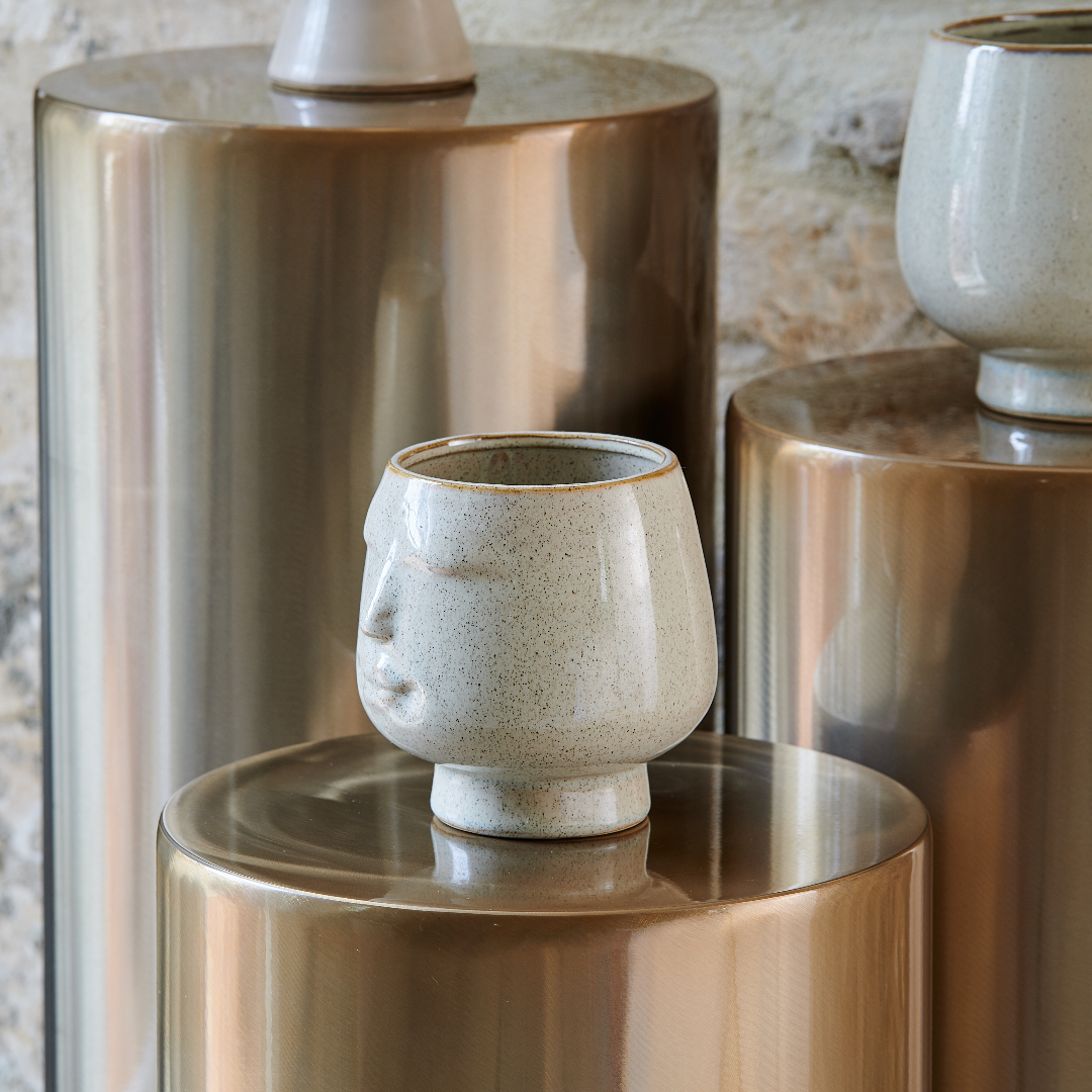 Vase en céramique représentant un visage, posé sur des supports en métal doré. Design contemporain et artisanal.