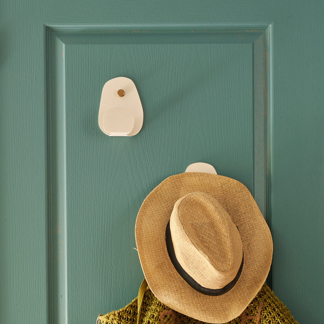 Patère design en acier blanc avec un chapeau de paille suspendu sur une porte bleue.