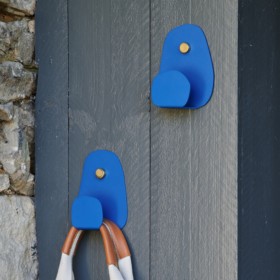 Patère Aphrodite en acier, design contemporain et épuré, installée sur un mur en bois gris, avec une corde accrochée.