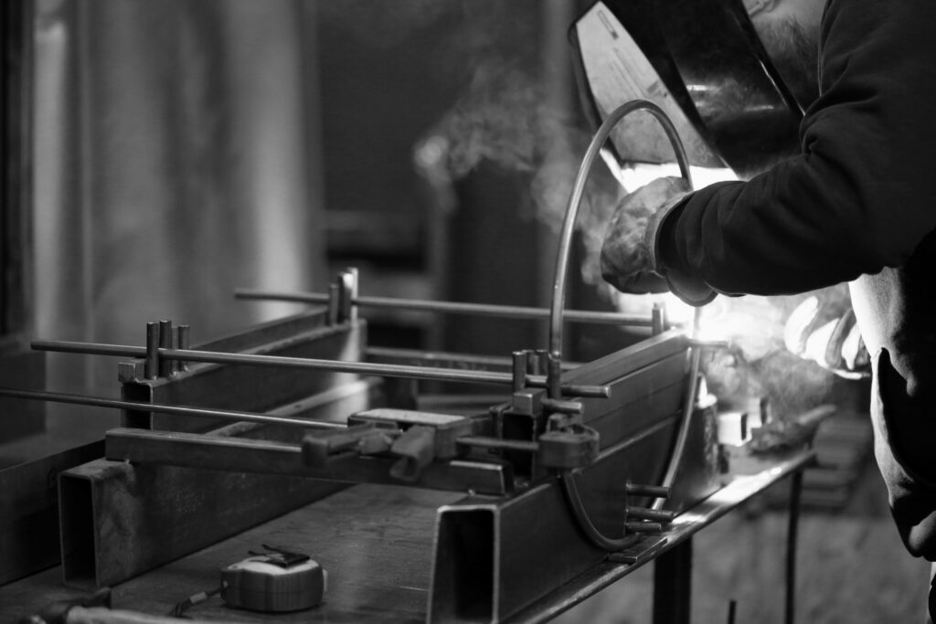 Artisan soudeur travaillant le métal dans l'atelier Héphaïstos, créant des meubles en acier avec soin.